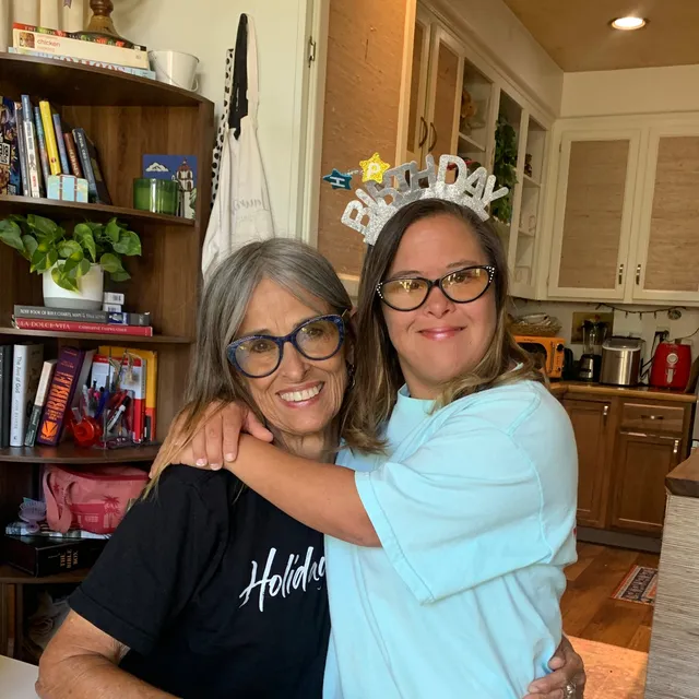 Two friends hugging at a birthday celebration, one wearing a sparkly birthday headband