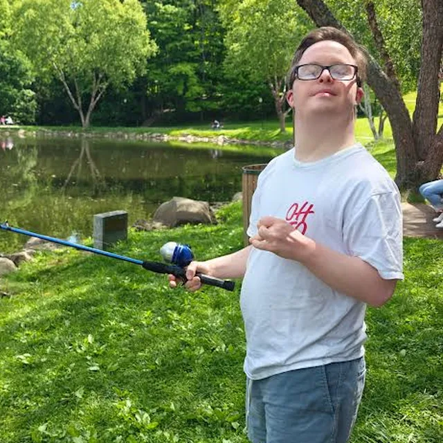 A young man in glasses fishing at a pond