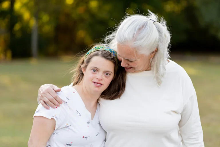 A young woman with Down syndrome sharing a warm hug with an older friend outdoors