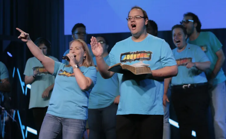 Friends singing and praising on stage, one holding an open Bible